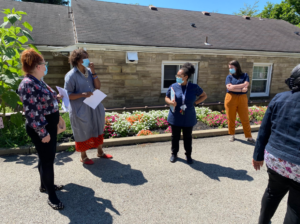 KaBloom judges gather and discuss the arrangement in front of red, white, and pink flower beds